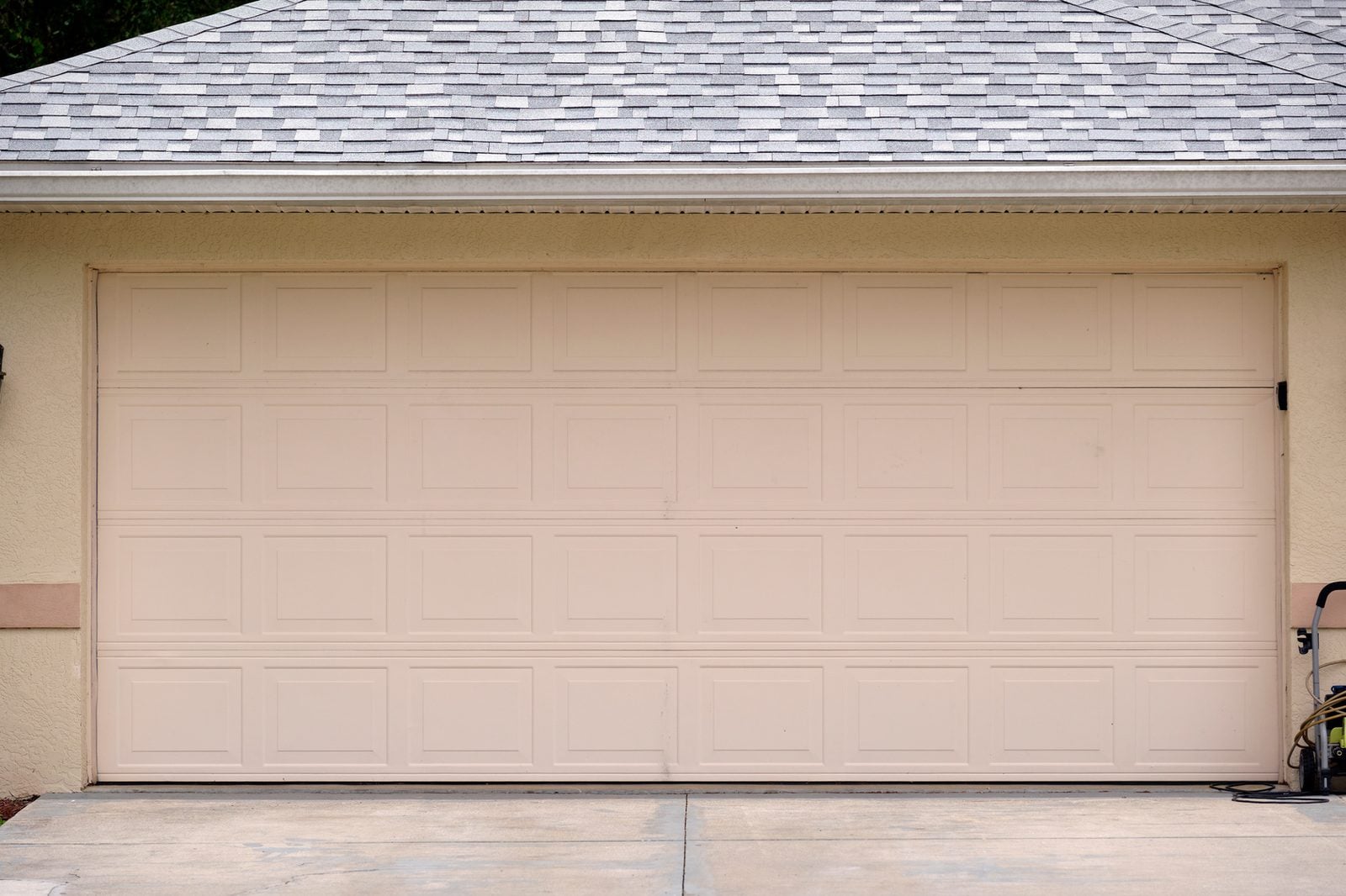 Wide beige double garage door above a concrete driveway